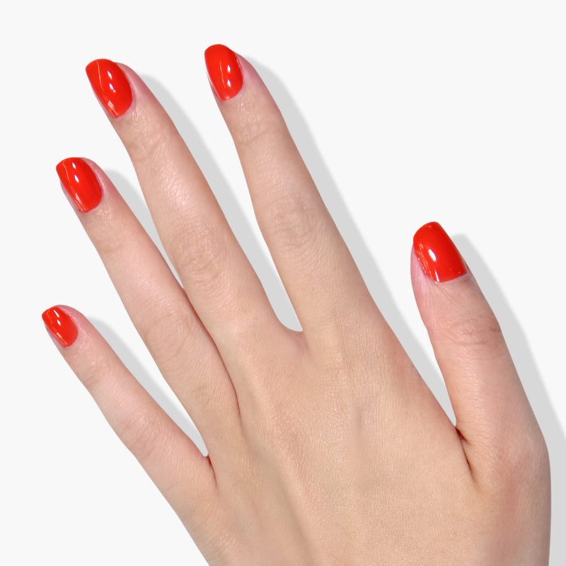 A hand with short, neatly manicured nails painted in a radiant citrusy orange crème named Camden Chic by LONDONTOWN against a white background.