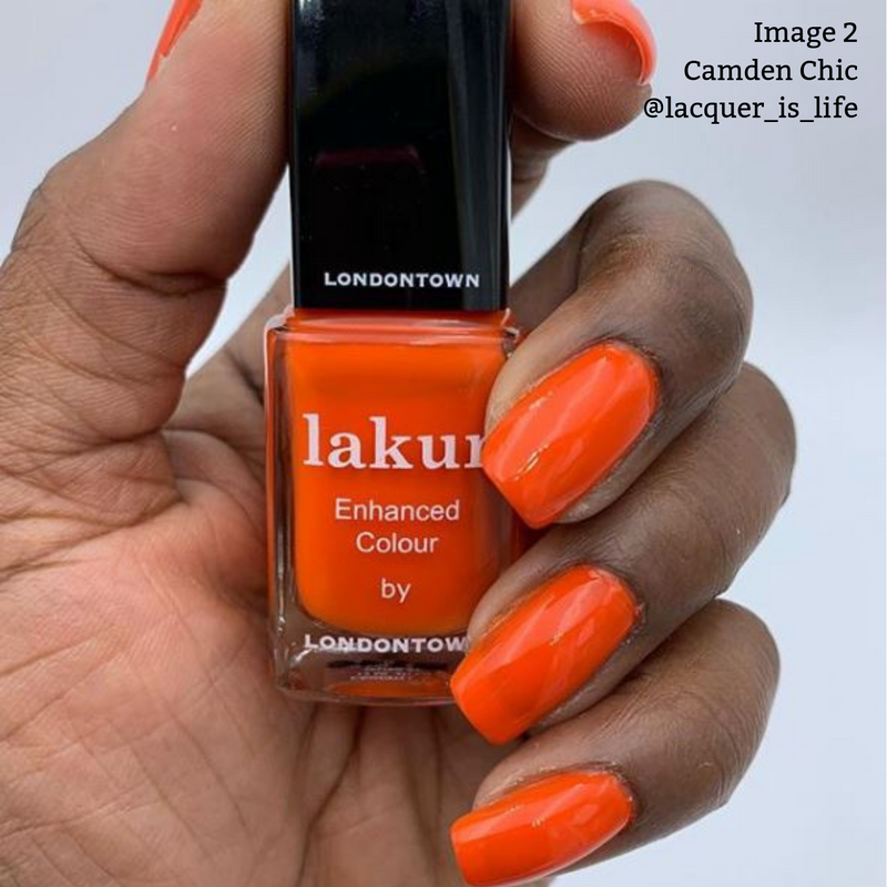 A hand with neatly manicured nails painted in a vibrant citrusy orange crème polish holds a bottle of LONDONTOWN Camden Chic nail polish. The vegan, cruelty-free formula ensures beauty with 16+ Free benefits.