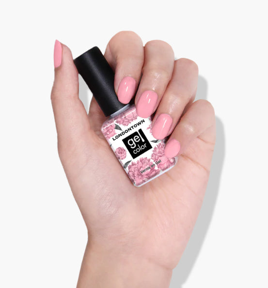 A hand with pink polished nails holds a bottle of LONDONTOWN's Candy Floss UV/LED Gel Color nail polish with a floral design label.