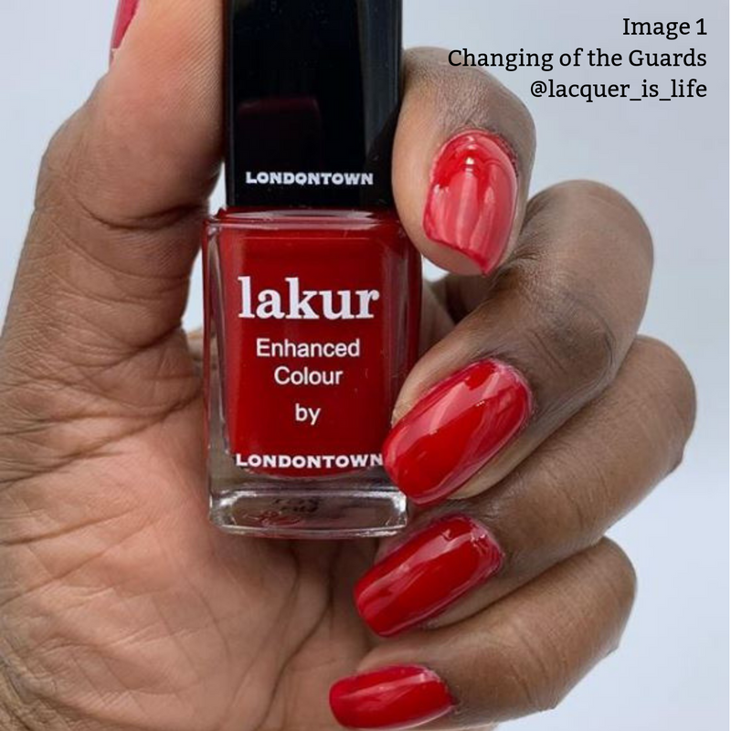 Close-up of a hand holding a bottle of LONDONTOWN's Changing of the Guards vegan nail polish in deep red crème, with the nails painted the same color. Text reads: "Image 1 Changing of the Guards @lacquer_is_life.