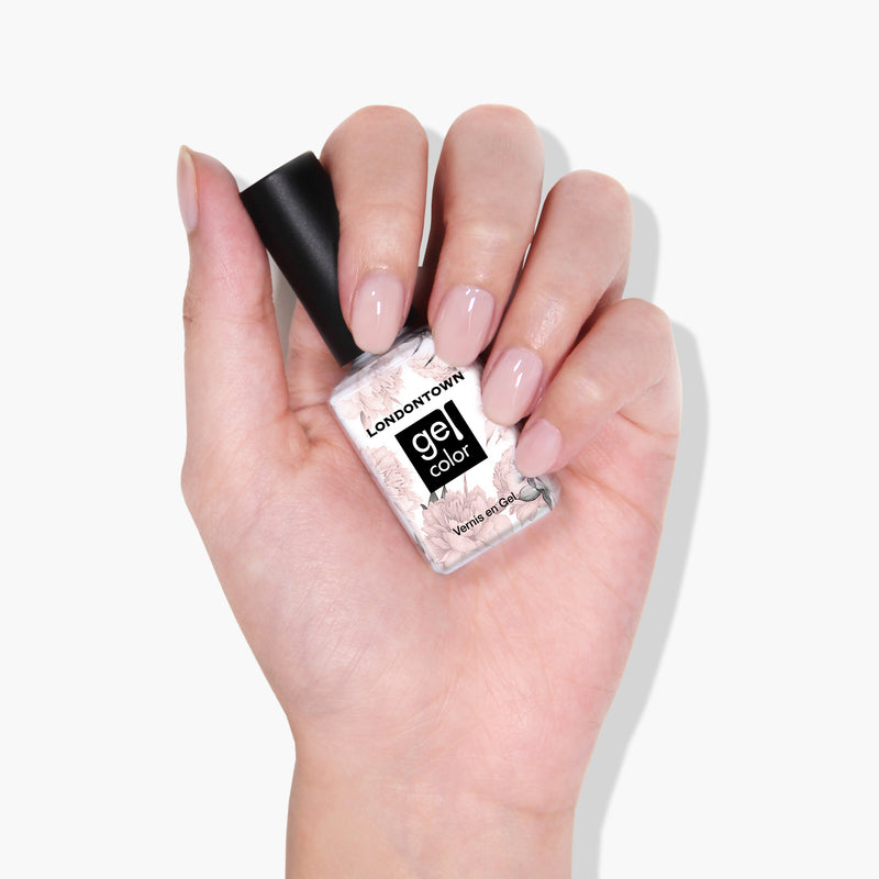 A hand with manicured nails holds a bottle of LONDONTOWN's Cheerio gel color nail polish in sheer neutral pink.