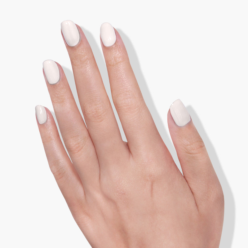 A hand with neatly trimmed fingernails painted in a glossy milky off-white crème nail polish, LONDONTOWN's Chelsea Porcelain, against a plain white background, highlighting the elegance of this vegan, cruelty-free nail polish.