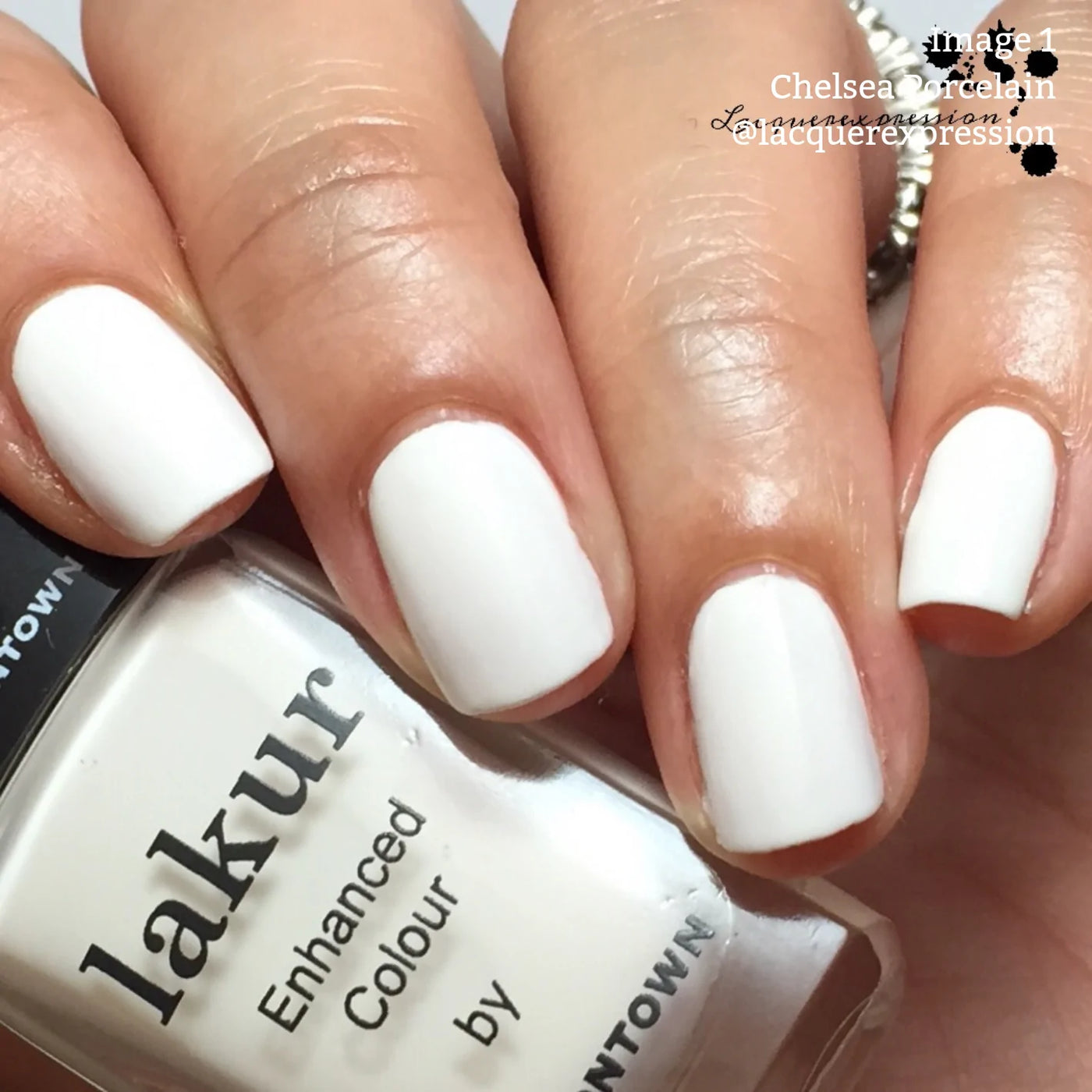 Close-up of a hand with neatly manicured nails painted in a milky off-white crème, holding a bottle of "Chelsea Porcelain (Professional)" vegan cruelty-free nail polish by LONDONTOWN.