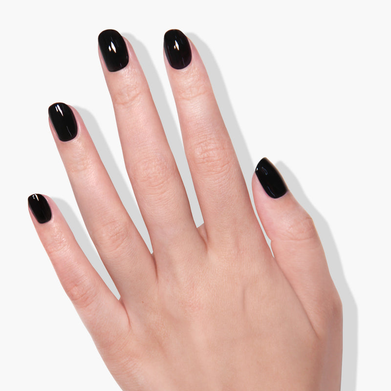 A human hand with short, rounded nails painted in LONDONTOWN's Chim Cher-ee jet black crème is shown against a white background, the streak-free finish accentuating the glossy surface.