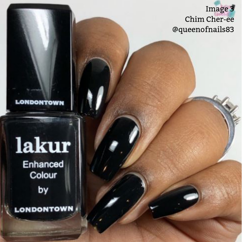 Close-up of a hand with long black manicured nails holding a bottle of LONDONTOWN's Chim Cher-ee Lakur Enhanced Colour vegan cruelty-free nail polish. A ring with a bow design is worn on the ring finger.