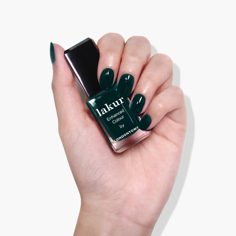 A hand holding a bottle of dark green nail polish labeled "Chivvy Along by LONDONTOWN." The nails are painted in the same shade of green, showcasing the cruelty-free, vegan beauty product.