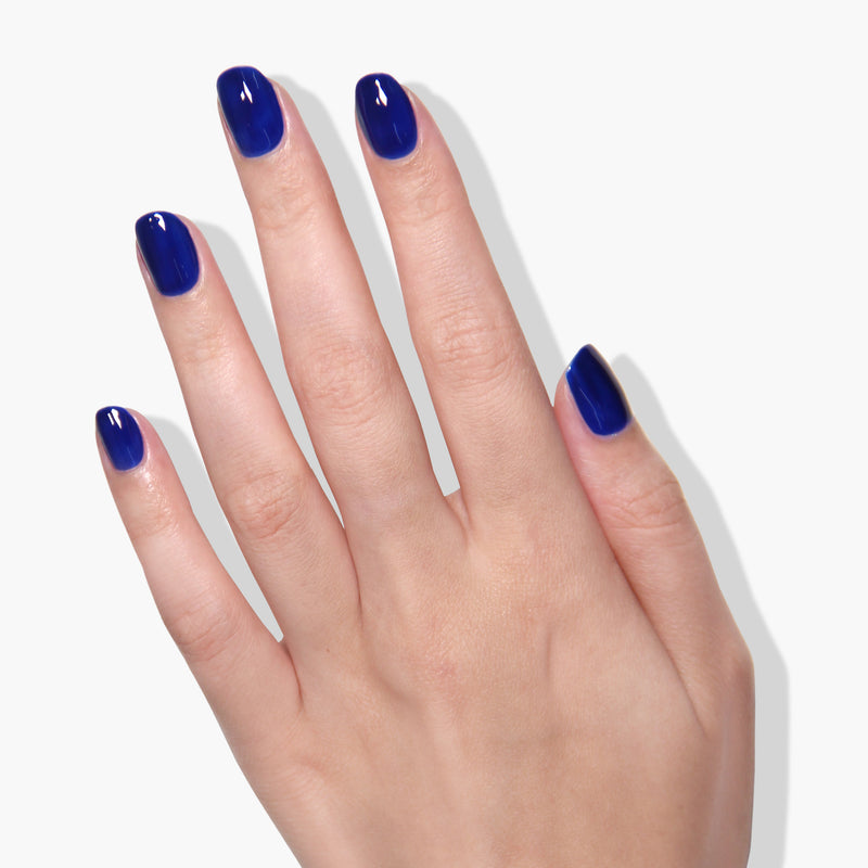 A hand with neatly trimmed nails, painted in LONDONTOWN's "Cocktail Hour," a glossy blue gel color that shimmers under UV/LED light, displayed against a white background.