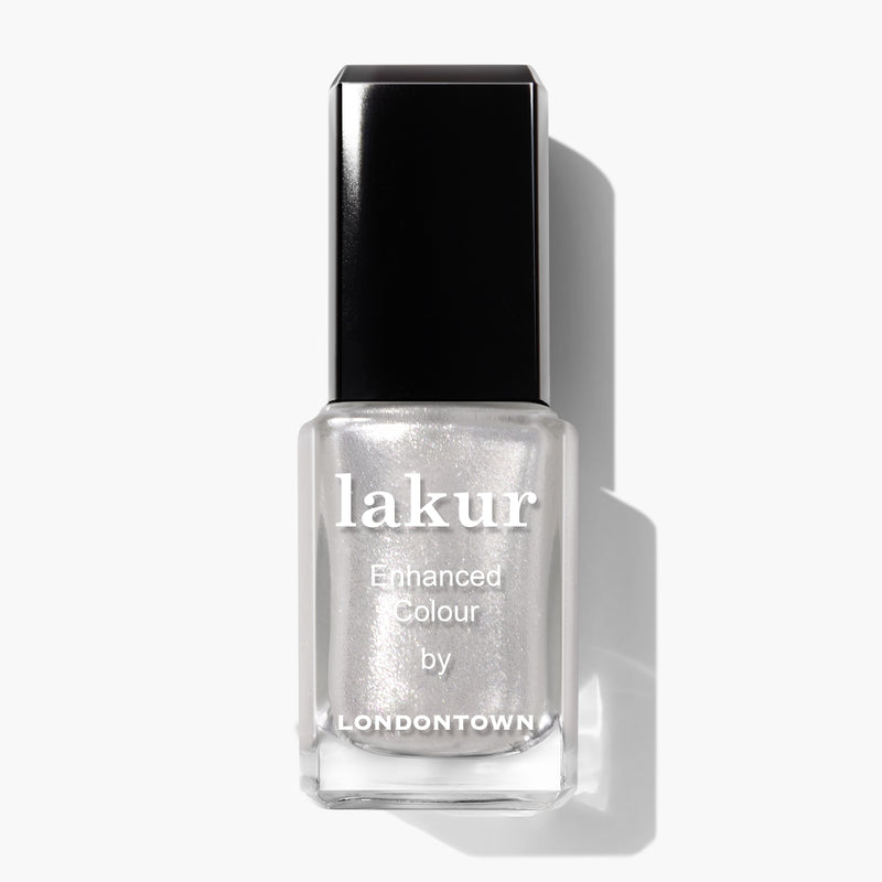 A bottle of LONDONTOWN Lakur Enhanced Colour nail polish in the shade "Coconut Crush," featuring a black cap and containing light silver shimmering polish infused with ultrafine glitter.