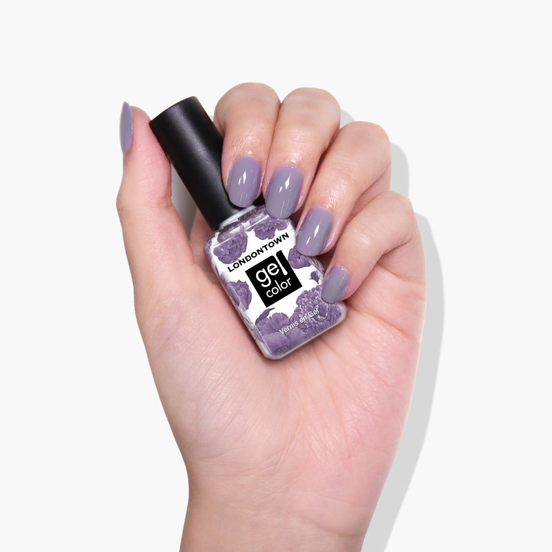 A hand holding a bottle of LONDONTOWN's Cozy Cashmere Gel Color nail polish in a purple crème shade. The nails, painted in a matching color, showcase the perfect gel manicure.