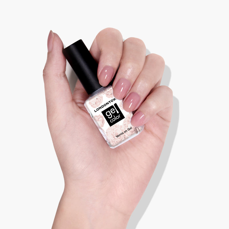 A hand with pink manicured nails is holding a bottle of LONDONTOWN Crowning Crumpet Gel Color nail polish, featuring color lock technology, against a white background.
