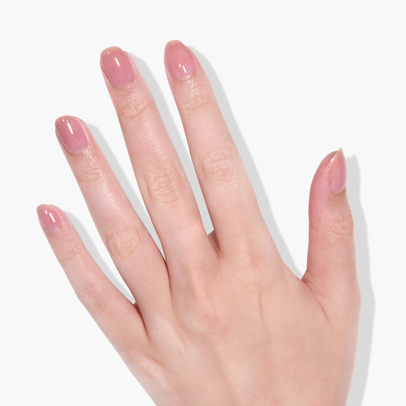A hand with light pink, sheer nude polished nails against a white background, showcasing a gel manicure using Crowning Crumpet by LONDONTOWN featuring color lock technology.