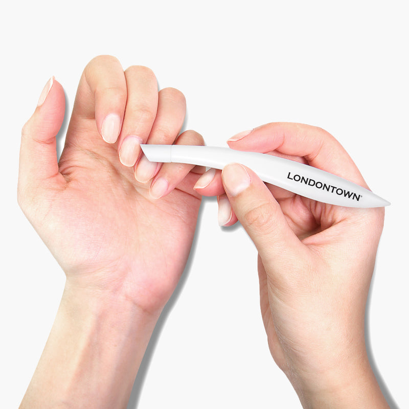 A person uses a LONDONTOWN Cuticle Pusher to care for their nails, holding the tool with one hand and shaping a nail on the other against a plain white background, achieving healthy-looking cuticles for a salon-quality manicure.