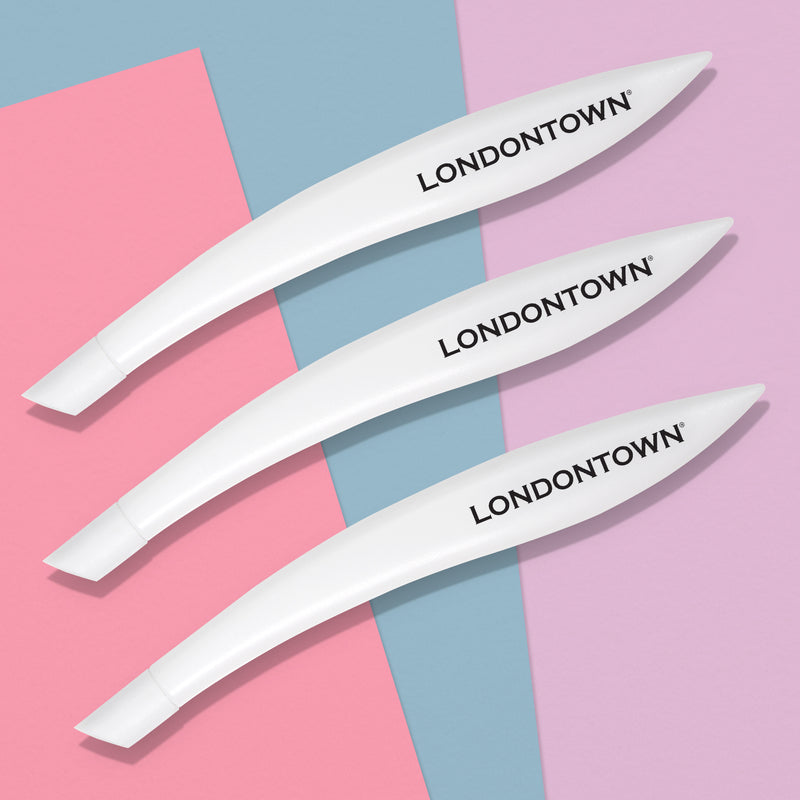 Three white cuticle pushers with the "LONDONTOWN" brand name printed on them are arranged diagonally on a background of pink, blue, and purple triangles, perfect for achieving salon-quality manicure results.