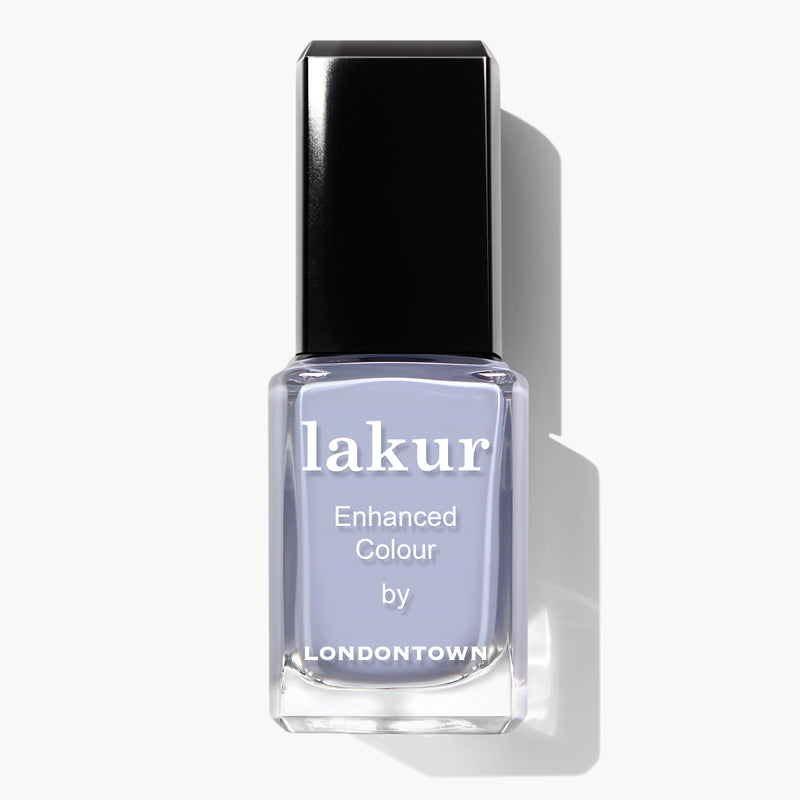A bottle of LONDONTOWN's Dainty Daze Lakur Enhanced Colour nail polish features a light lavender shade with periwinkle blue undertones and a black cap. This 16+ Free, vegan, and cruelty-free formula ensures both beauty and ethical standards are met.