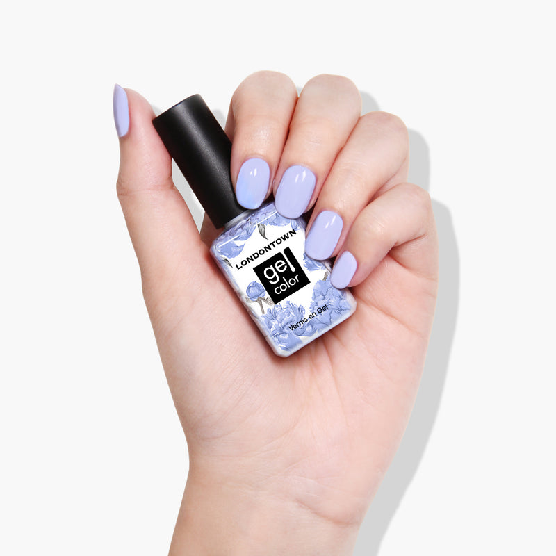 A hand with light purple nail polish holds a bottle of LONDONTOWN's Dainty Daze vegan, cruelty-free gel color nail polish.