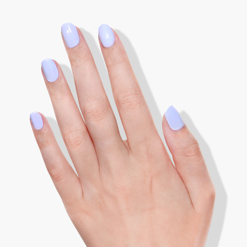 A hand with short, glossy nails painted in LONDONTOWN's Dainty Daze periwinkle blue nail polish is shown against a white background.