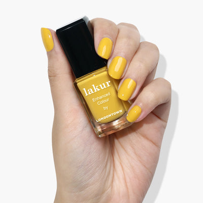 A hand with cheerful canary yellow nail polish holds a bottle of LONDONTOWN Daisy Chain (Professional) nail polish in a matching shade, providing an instant mood boost.