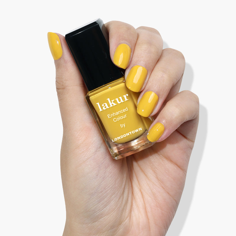 A hand with cheerful, yellow-painted nails holds a bottle of canary yellow nail polish labeled "Daisy Chain by LONDONTOWN.