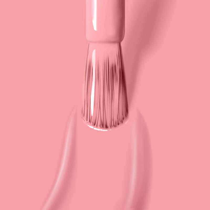 Close-up of a brush applying Desert Flower nail polish by LONDONTOWN on a matching pink background, showcasing the vibrant hue of this vegan, cruelty-free choice.