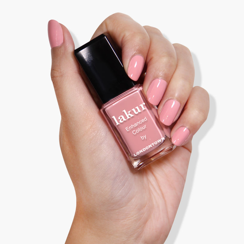 A hand with neatly manicured nails holds a bottle of LONDONTOWN's Desert Flower nail polish, a vegan, cruelty-free option perfect for any occasion.