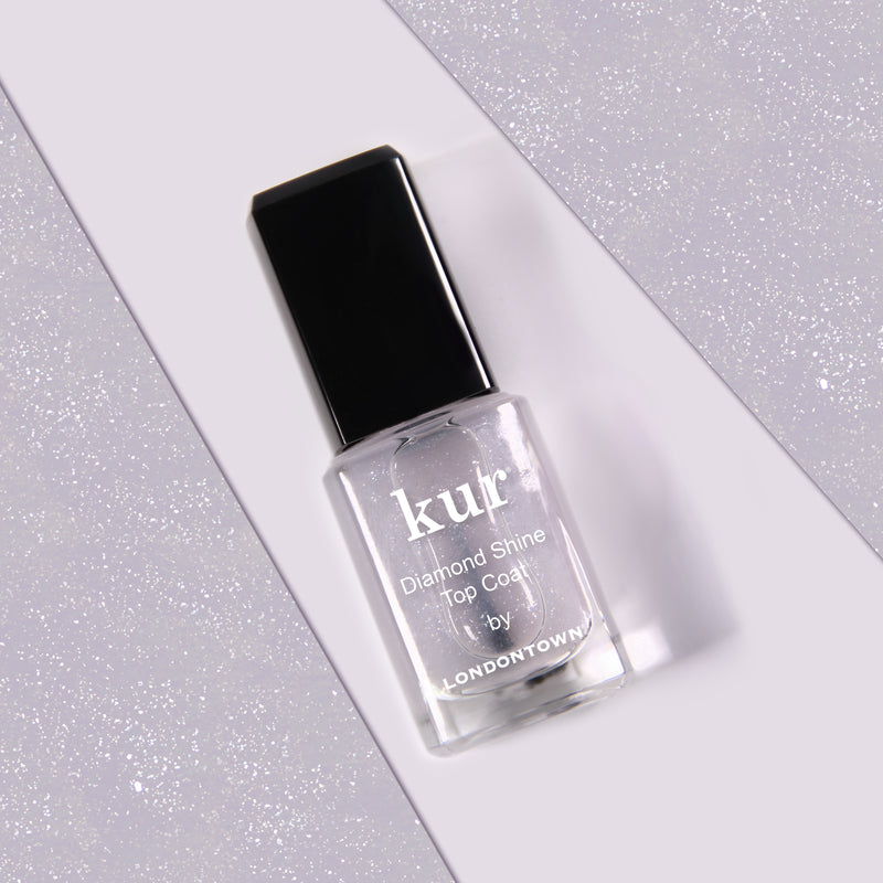 A bottle of LONDONTOWN's Diamond Shine Top Coat with a black cap on a glittery gray background, offering extended wear for an enduring finish.
