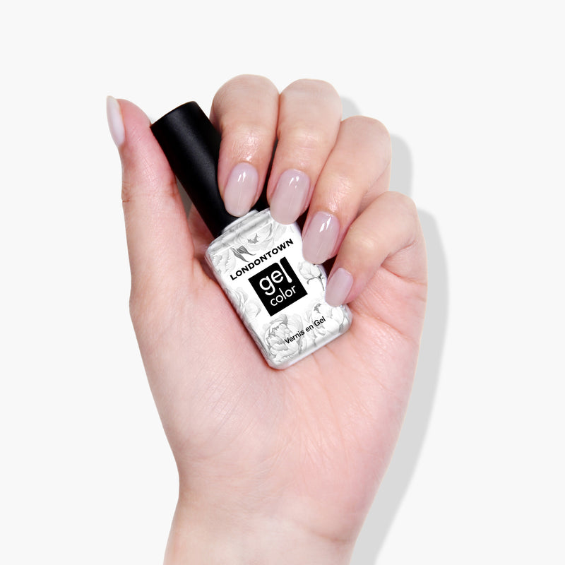 A hand holding a bottle of LONDONTOWN's Doilies Gel Color nail polish with light pink painted nails against a white background, perfect for achieving a sheer white gel manicure.