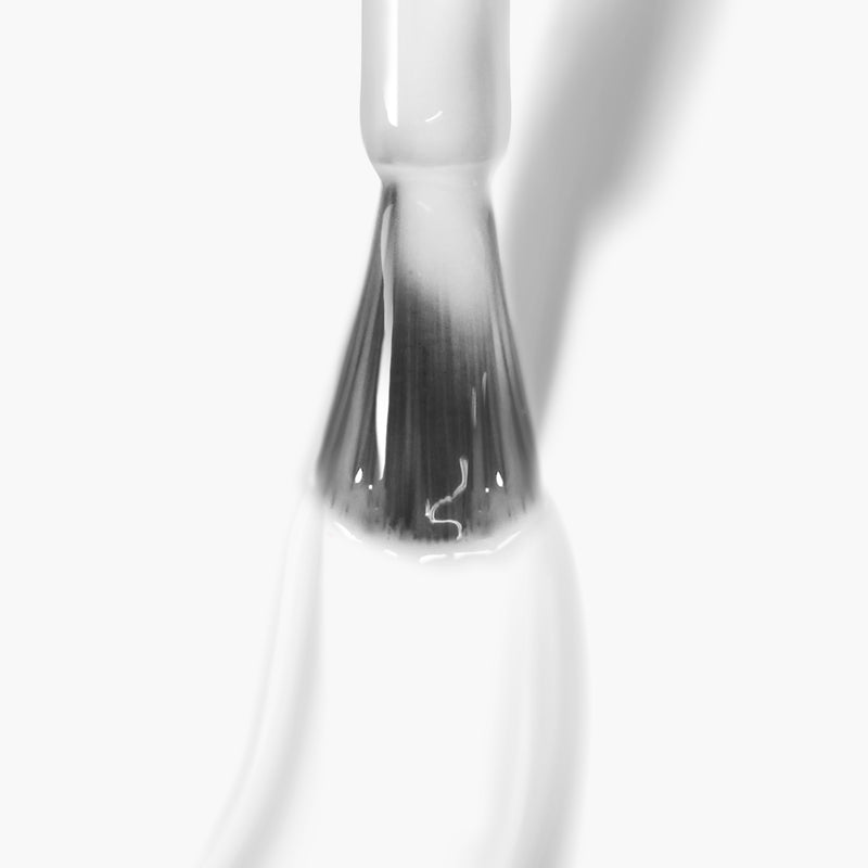 Close-up view of a brush in a clear bottle with opaque liquid, possibly LONDONTOWN's Doilies sheer white nail polish. The brush appears to be freshly dipped and coated with the liquid, ideal for achieving a gel manicure cured under UV/LED light.