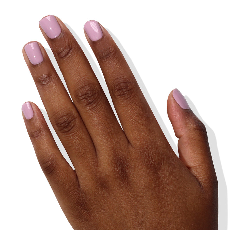 A hand with medium skin tone displaying short, rounded nails painted in LONDONTOWN's delicate lilac nail polish, Dolly Mix, rests against a plain white background. The shade is from our vegan cruelty-free collection, ensuring beauty without compromise.