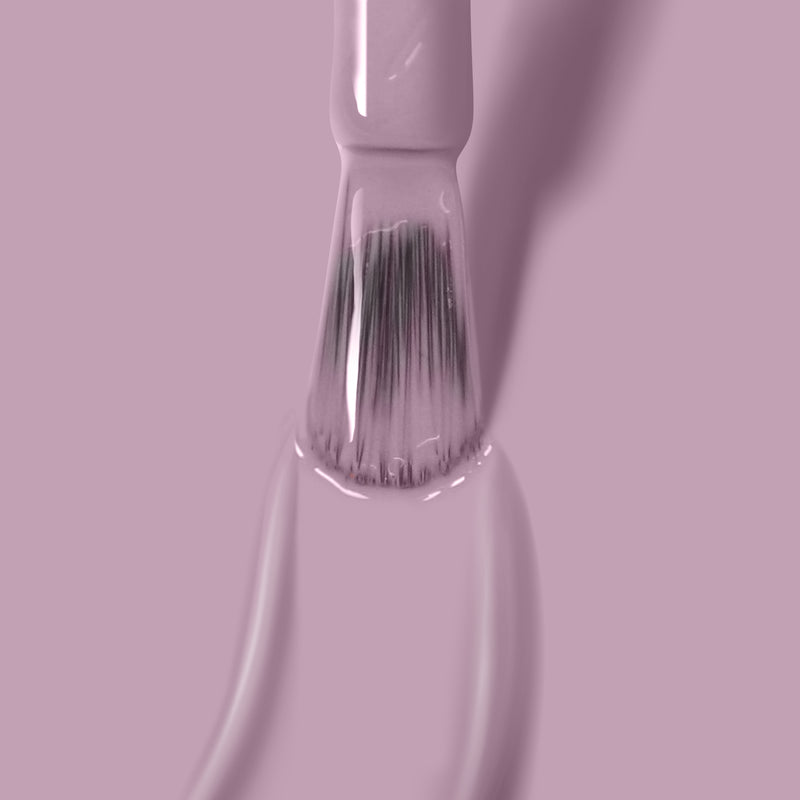 Close-up of LONDONTOWN's vegan, cruelty-free Dolly Mix nail polish brush dipped in light pink polish, with droplets forming at the bristles' tips, against a matching pink background.