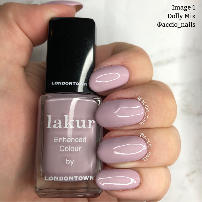 Hand holding a black-capped bottle of "Dolly Mix" nail polish by LONDONTOWN in a light mauve shade, showcasing polished nails of the same color. This 16+ free, vegan cruelty-free lilac nail polish is the perfect touch for any manicure.