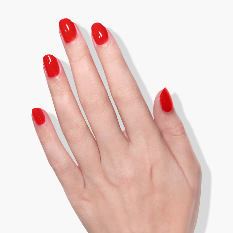 A hand with manicured nails painted in Double the Deck, a vibrant true red crème from LONDONTOWN, is shown against a white background, highlighting the vegan cruelty-free formula.