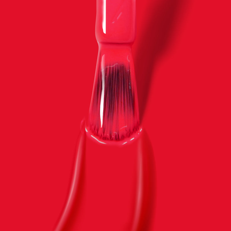 A paintbrush coated with bright red paint stands against a vibrant backdrop, reminiscent of the bold hues in LONDONTOWN's Down to Dilly polish.