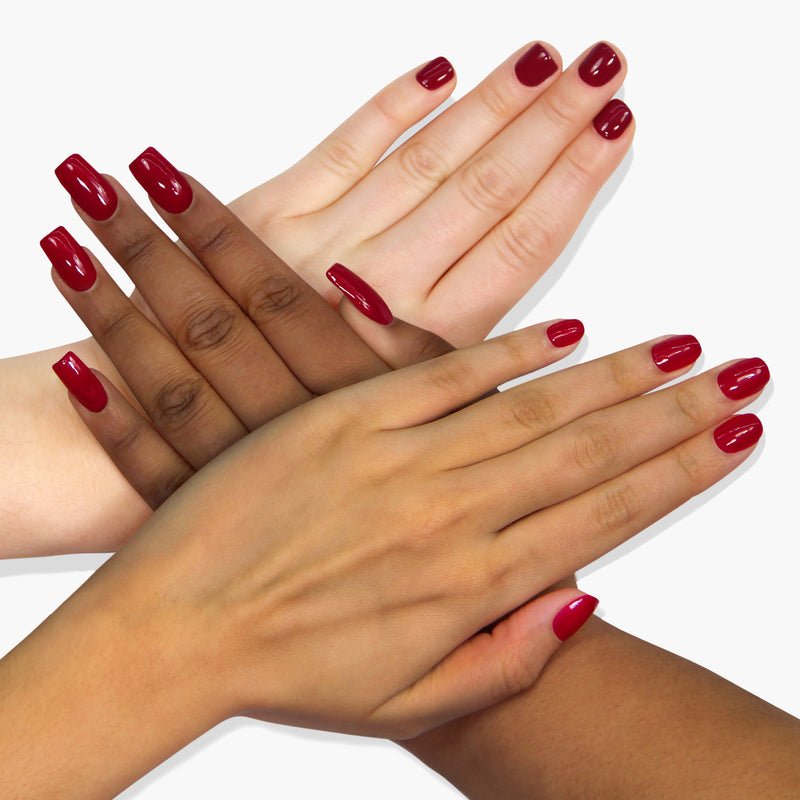 Four hands of varying skin tones with nails painted in a sophisticated amaranth purple shade called Dragon Fruit by LONDONTOWN are placed overlapping on a white background.