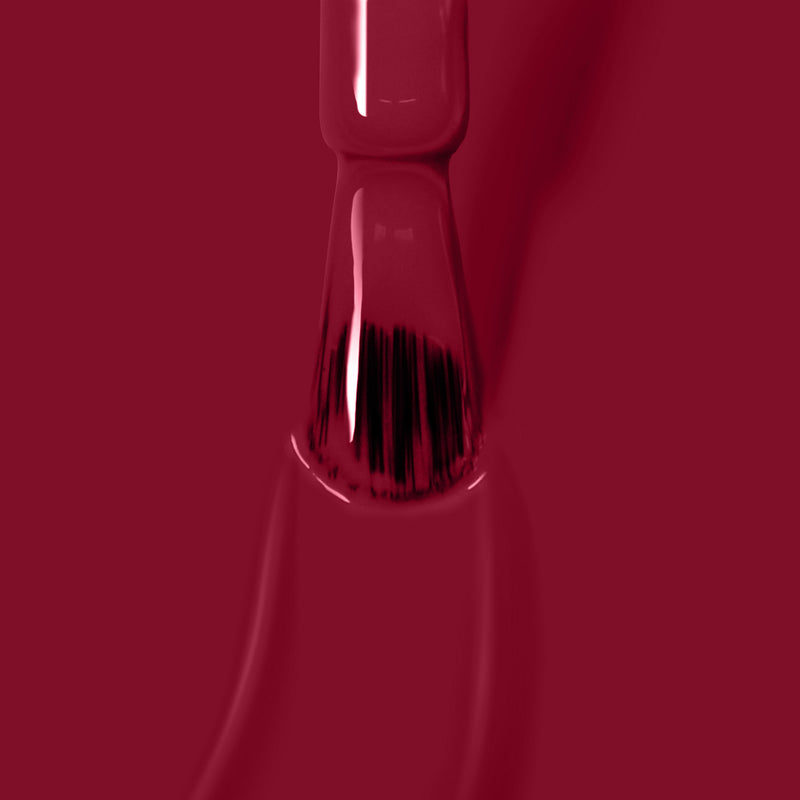 Close-up of a nail polish brush applying glossy Dragon Fruit, a vegan and cruelty-free nail polish by LONDONTOWN, on a surface.