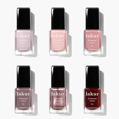 Six bottles of LONDONTOWN’s Essential Palette nail polish are arranged in two rows, featuring a beloved neutrals collection with shades from light pink and nude to metallic pink and deep red.