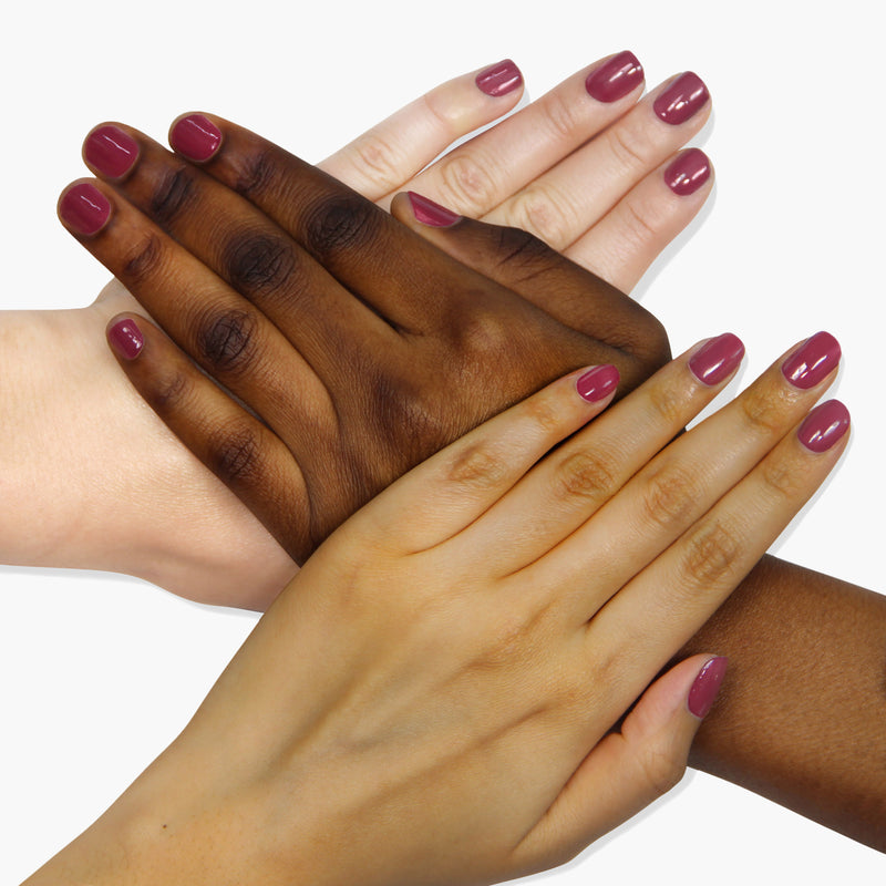 Four hands of different skin tones, each adorned with LONDONTOWN's "Fig Jam" mauve-tinged purple nail polish, are stacked on top of each other against a white background.