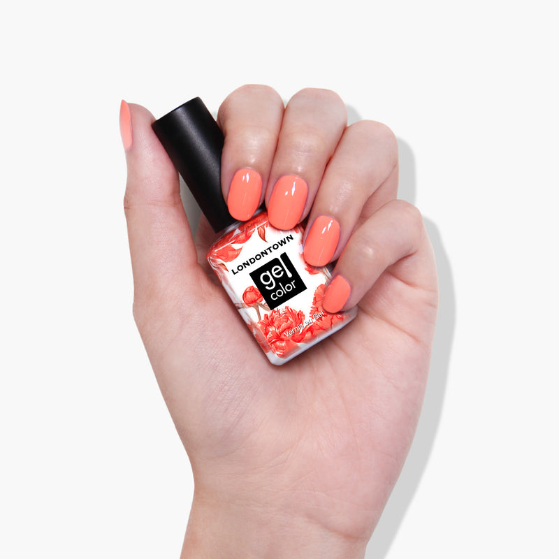 A hand with painted nails holds a bottle of LONDONTOWN's Flashback gel color nail polish in a vibrant neon orange shade, perfect for use with UV/LED light.