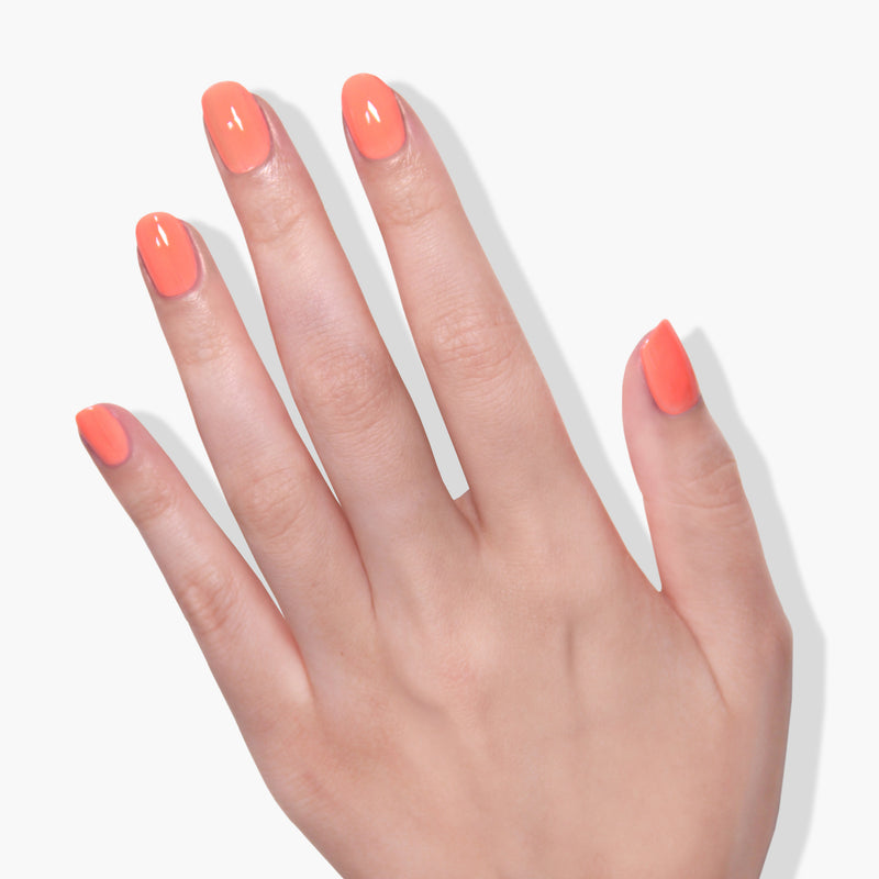 A hand with LONDONTOWN's Flashback gel color neon orange nail polish on a white background.
