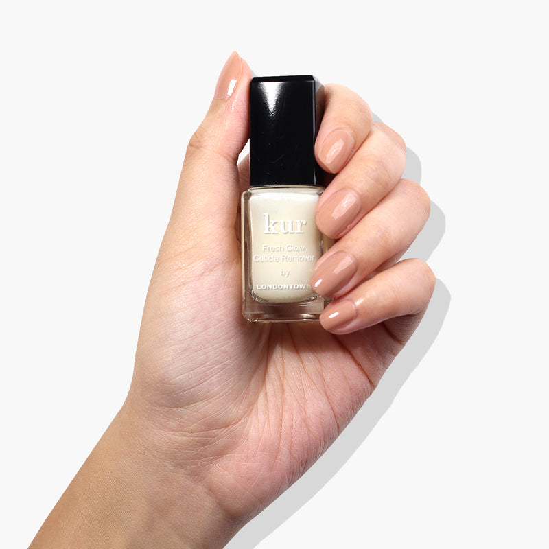 A hand with manicured nails holds a bottle of Fresh Glow Cuticle Remover by LONDONTOWN, the perfect solution for tackling overgrown cuticles, against a plain white background.