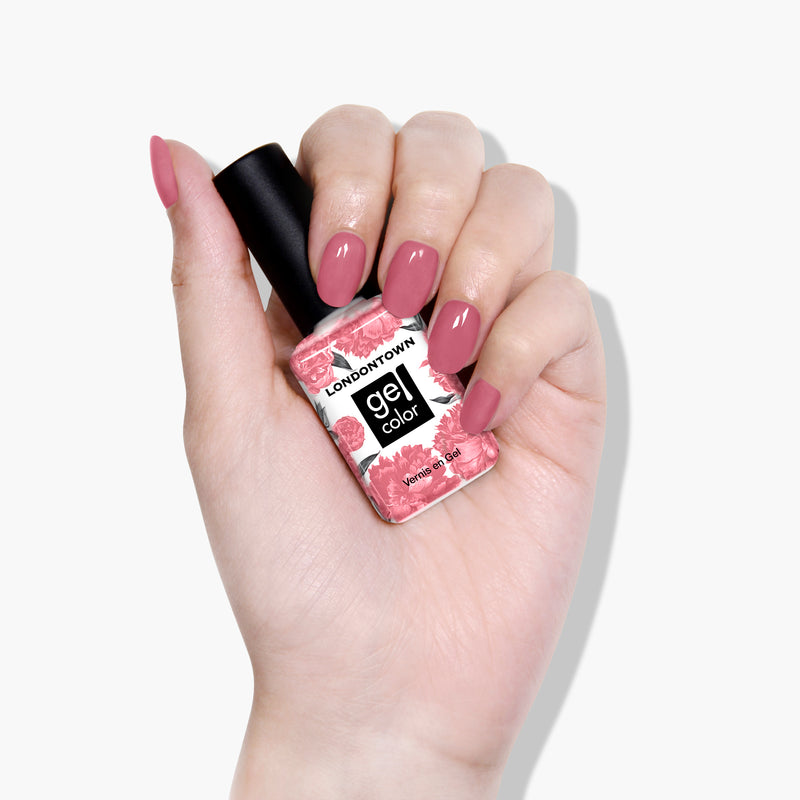 A hand with neatly manicured clay rose nails holds a bottle of LONDONTOWN's Mojave Mauve gel nail polish against a plain white background, exuding a sophisticated, ladylike charm.