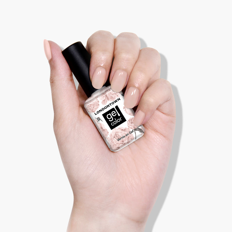 A hand holding a bottle of LONDONTOWN's Uncovered UV/LED Gel Color nail polish with flawless, nude-colored nails, set against a plain white background.