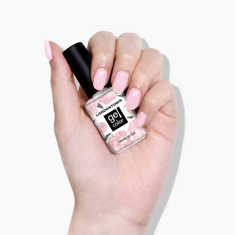 A hand with light pink polished nails holds a bottle of LONDONTOWN's Waterloo Sunset UV/LED Gel Color nail polish, featuring a high-shine formula.