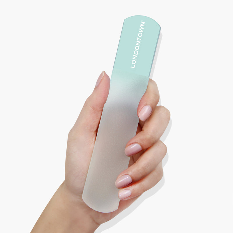 Hand holding a transparent glass foot file with a mint-green handle labeled "LONDONTOWN," known for its gentle yet effective smoothing abilities.