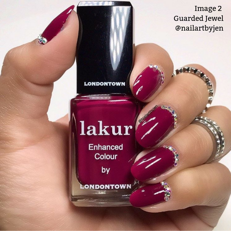 A hand with deep maroon crème painted nails adorned with rhinestones holds a bottle of LONDONTOWN Guarded Jewel polish. Text reads: "Image 2 Guarded Jewel @nailartbyjen".
