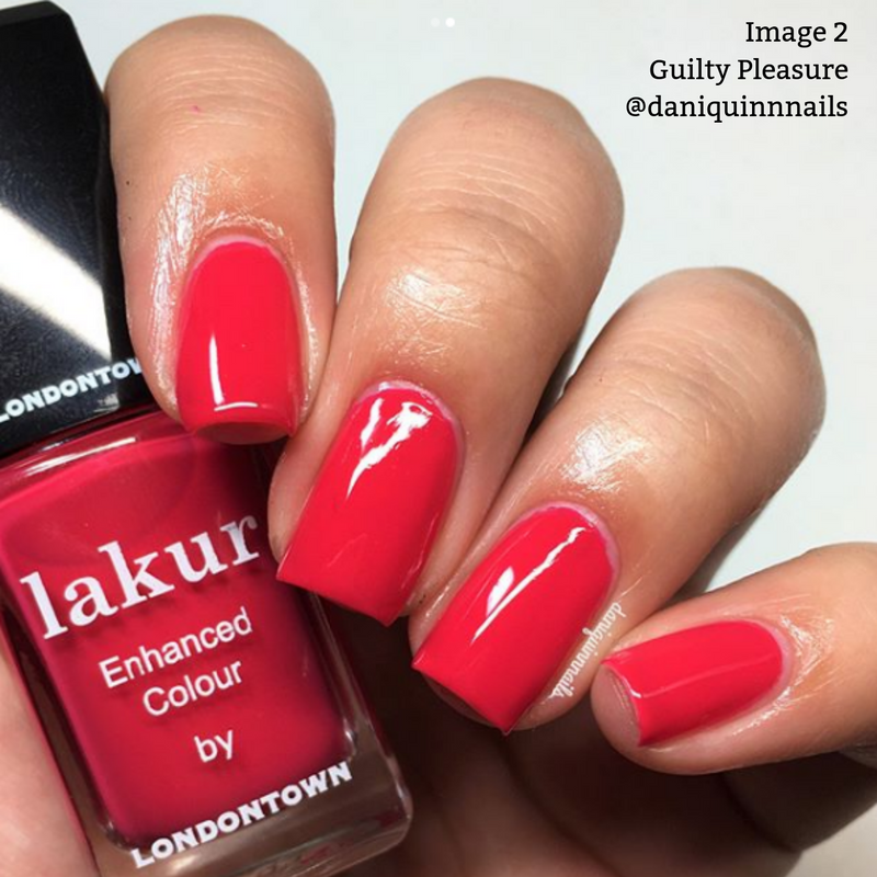 A hand with freshly manicured nails painted in a shiny red shade is shown holding a bottle of LONDONTOWN's "Guilty Pleasure" lakur nail polish, which is both formaldehyde-free and vegan.