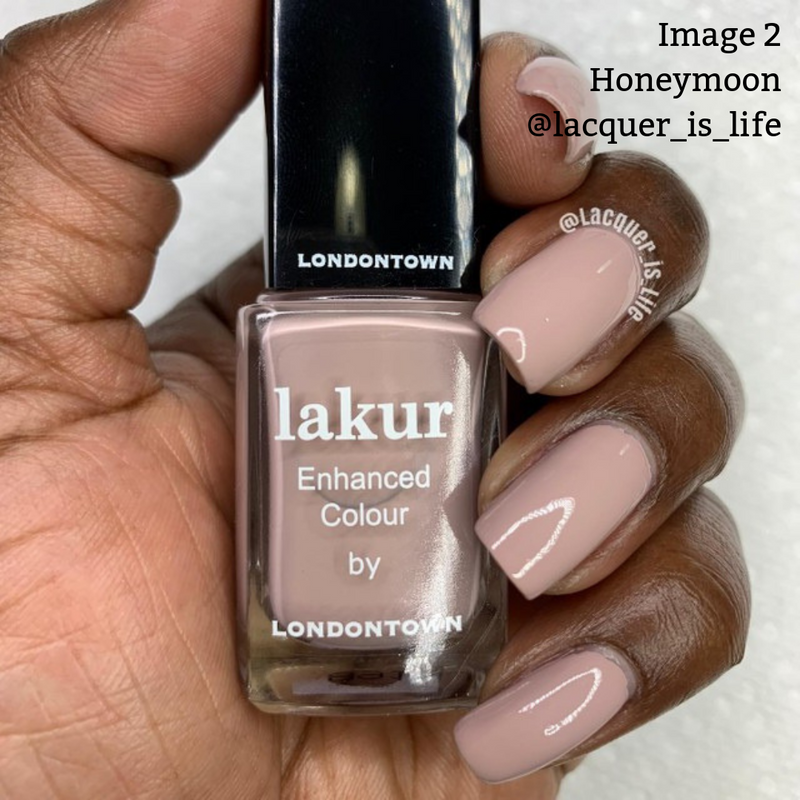 A hand holding a bottle of LONDONTOWN's Honeymoon nail polish—a cruelty-free, vegan formula—in a nude shade. The nails appear to be painted with the same color. Username @lacquer_is_life is visible in the background.