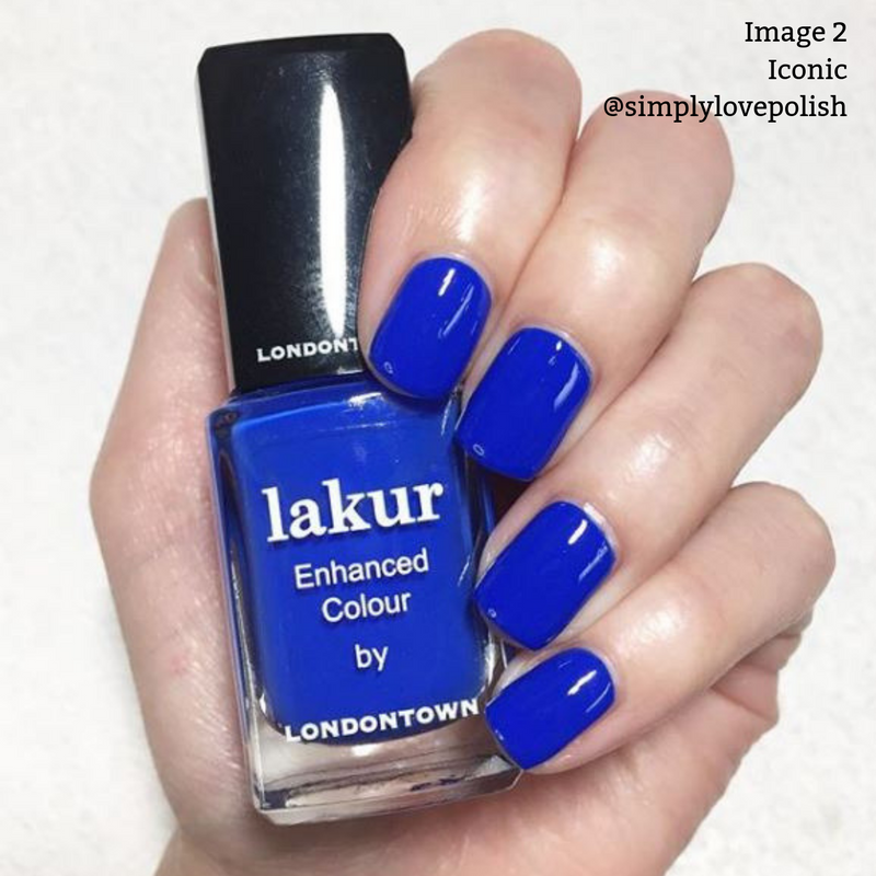 A hand with bright blue polished nails holds a bottle of LONDONTOWN Iconic Lakur Enhanced Colour nail polish in the same shade. The bottle's label is clearly visible. This vegan, cruelty-free formula won the 2019 Allure Best of Beauty Award. Text reads "Image 2 Iconic @simplylovepolish".