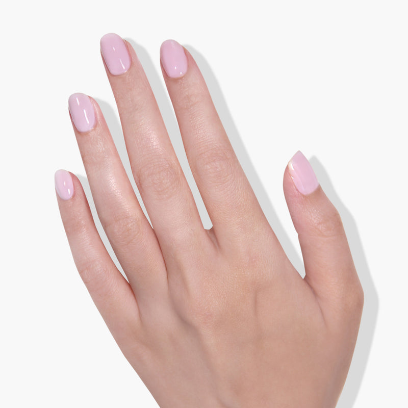 A close-up of a hand with neatly manicured fingernails painted in "Invisible Crown," a soft sheer pink gel color by LONDONTOWN, shown against a white background.