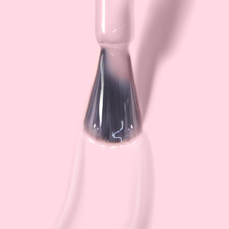 Close-up of a LONDONTOWN Invisible Crown nail polish brush with soft sheer pink gel color being applied against a pale pink background.