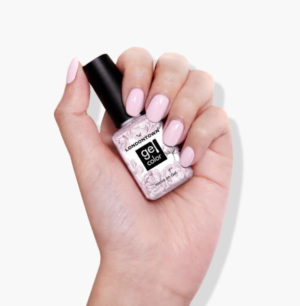 A hand with pink nail polish holds a bottle of LONDONTOWN's Jane Austen UV/LED Gel Color nail polish against a white background, showcasing its vegan, cruelty-free, self-leveling high-shine formula.